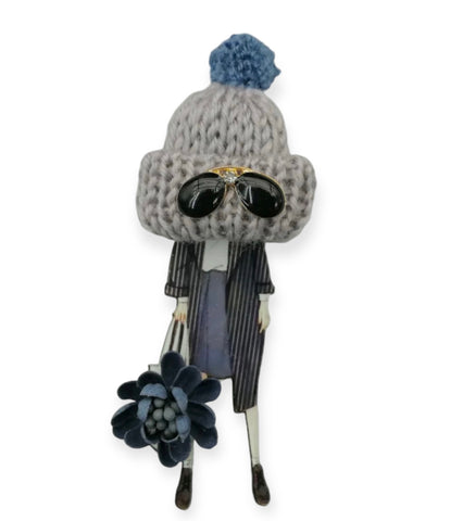 Spilla con modella e cappellino in lana grigio con ponpon e occhiali da sole